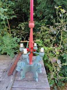 a red and blue candle holder sitting on top of a wooden table next to bushes