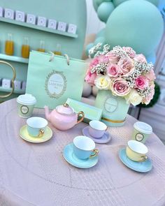 a table topped with cups and saucers next to a vase filled with pink roses