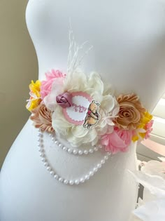 a white mannequin wearing a pink and yellow flower belt with pearls on it