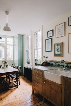 a kitchen with wooden floors and white walls is pictured in this image, there are many framed pictures on the wall