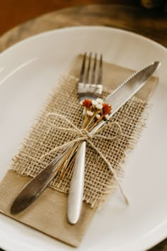 a white plate topped with two forks and a napkin wrapped in burlap next to silverware