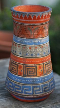 an orange and blue vase sitting on top of a wooden table