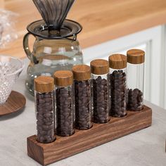 an assortment of coffee beans in glass bottles on a wooden stand next to a pitcher