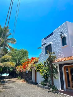 a white house sitting on the side of a road next to palm trees and flowers