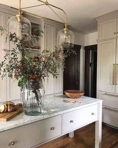 a kitchen with white cabinets and marble counter tops, vases filled with flowers on the island