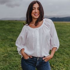 a woman standing in a field with her hands on her hips and looking at the camera