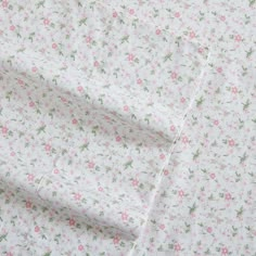 a white sheet with pink and green flowers is folded on top of a bed spread