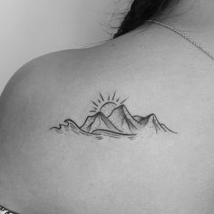 the back of a woman's shoulder with a mountain and sun tattoo