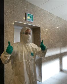 a man in a white suit and green gloves standing next to a mirror giving the thumbs up