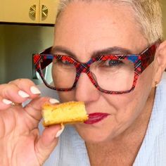 an older woman wearing glasses is eating something with her fingers and looking at the camera