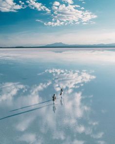 two people walking across a large body of water under a blue sky with white clouds