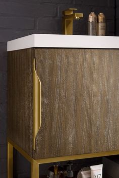 a wooden cabinet with gold handles and white counter top next to a black brick wall