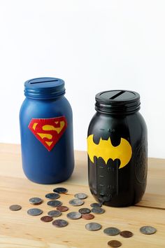 two mason jars with superman and batman logos on them, next to some pennets