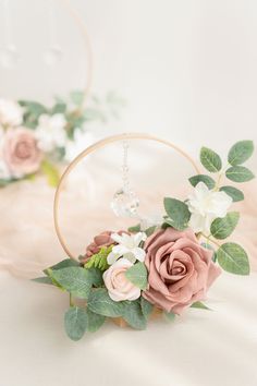 a pink rose and white flowers in a hoop with greenery on the side, sitting on a bed