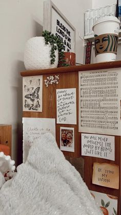 a white blanket on top of a bed next to a wooden shelf with pictures and other items