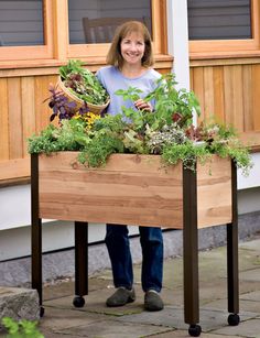 a woman standing in front of a wooden box filled with plants and vegetables that reads, standing garden is easy on your back