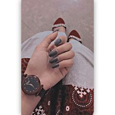 a woman's hand with grey nail polish holding a watch