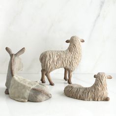 three ceramic sheep sitting next to each other on a white counter top with a marble wall in the background