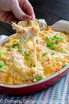 a person dipping some food into a casserole dish with green onions and cheese