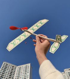 a hand is holding a toy airplane in the air with two buildings behind it and a blue sky