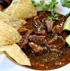 a white plate topped with meat and tortilla chips next to lime wedges