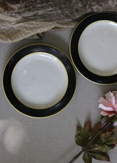 two black and white plates sitting on top of a table next to a pink flower