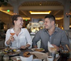 two people sitting at a table with food and drinks in front of them, smiling