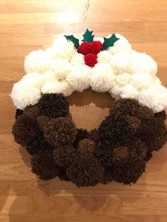 a christmas wreath with pom - poms and holly on it sitting on a wooden floor