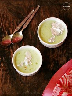 two white bowls filled with soup on top of a wooden table next to spoons