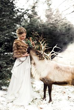 a woman standing next to a reindeer in the snow