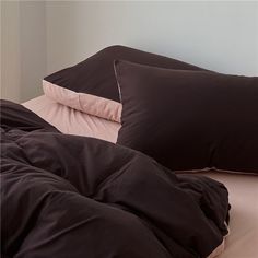 two black pillows and one pink pillow on a bed