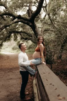 a pregnant woman sitting on top of a wooden bench next to a man