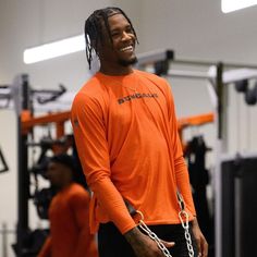 a man in an orange shirt with chains around his neck and hands behind his back