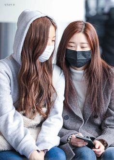 two young women wearing face masks while looking at their cell phones