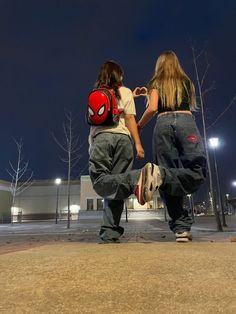 two people are walking down the street at night with backpacks on their back and one is holding his hand