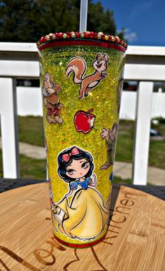 a glass with an image of snow white and the seven dwarfs on it sitting on top of a wooden table