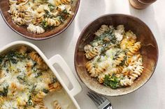 two bowls filled with pasta and spinach on top of a white cloth next to a fork