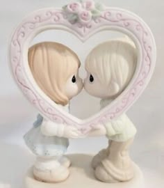 a figurine of two children kissing in front of a heart shaped frame with flowers