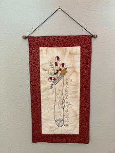 a wall hanging on the side of a white wall with a red frame holding a vase filled with flowers