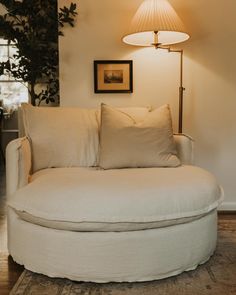 a white round couch with pillows on it in a living room next to a lamp