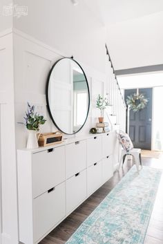 a room with white furniture and a large mirror on the wall above it, along with a blue rug