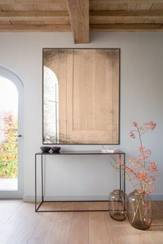 a mirror and vase with flowers in it on a table next to a door that leads to an arched window