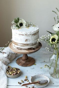 a white cake sitting on top of a wooden table next to vases filled with flowers