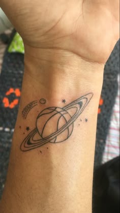 a small saturn tattoo on the wrist is shown in black and grey ink with stars around it