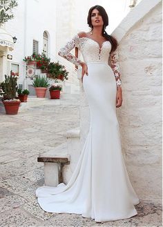 a woman in a white wedding dress leaning against a wall with her hands on her hips