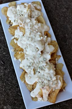 a white plate topped with cheesy potato chips covered in ranch dressing on top of a table