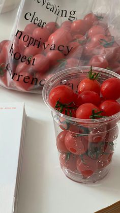 a plastic container filled with lots of red tomatoes next to a bag of clear clams