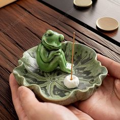 a person holding a green frog figurine on a leaf shaped dish with toothpicks in it