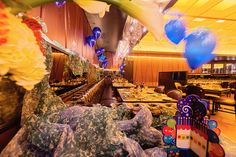 an indoor dining area with many tables and chairs covered in cloths, flowers and balloons