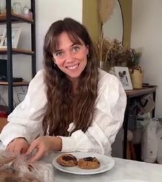 a woman sitting at a table in front of a plate of cookies and doughnuts